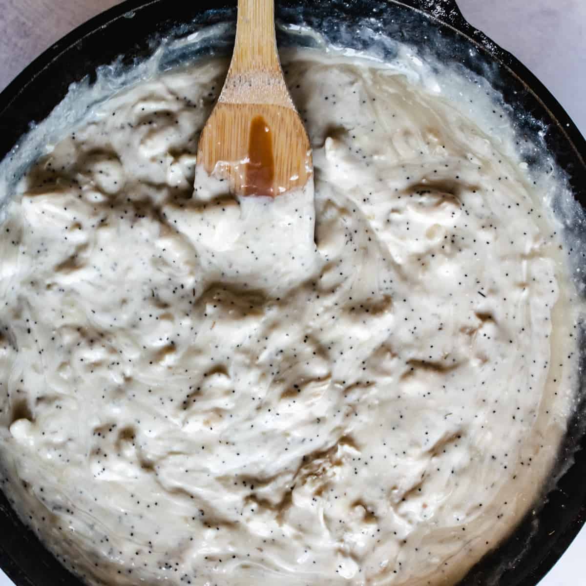 cast iron skillet with creamy chicken poppy seed casserole filling being stirred with wooden spatula