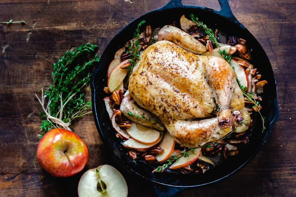 Roasted chicken in a cast iron skillet surrounded by fresh apples an pecans.