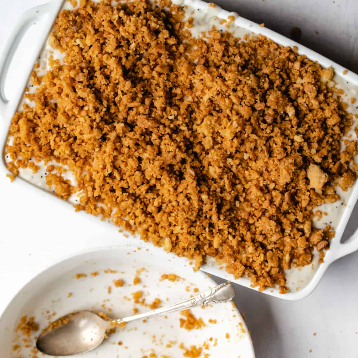 white casserole dish covered with cracker crumb topping next to empty bowl of crumbs
