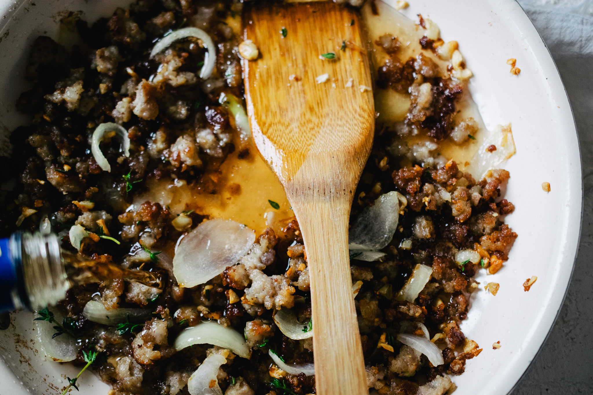 DSC_0203 ceramic skillet with browned sausage, onion and garlic being deglazed with sherry and a wooden spatula