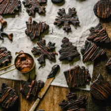 Chocolate Mint Sandwich Cookies with gold measuring cup of melted chocolate for drizzling on a piece of wax paper and antique butter knife with ganache smear