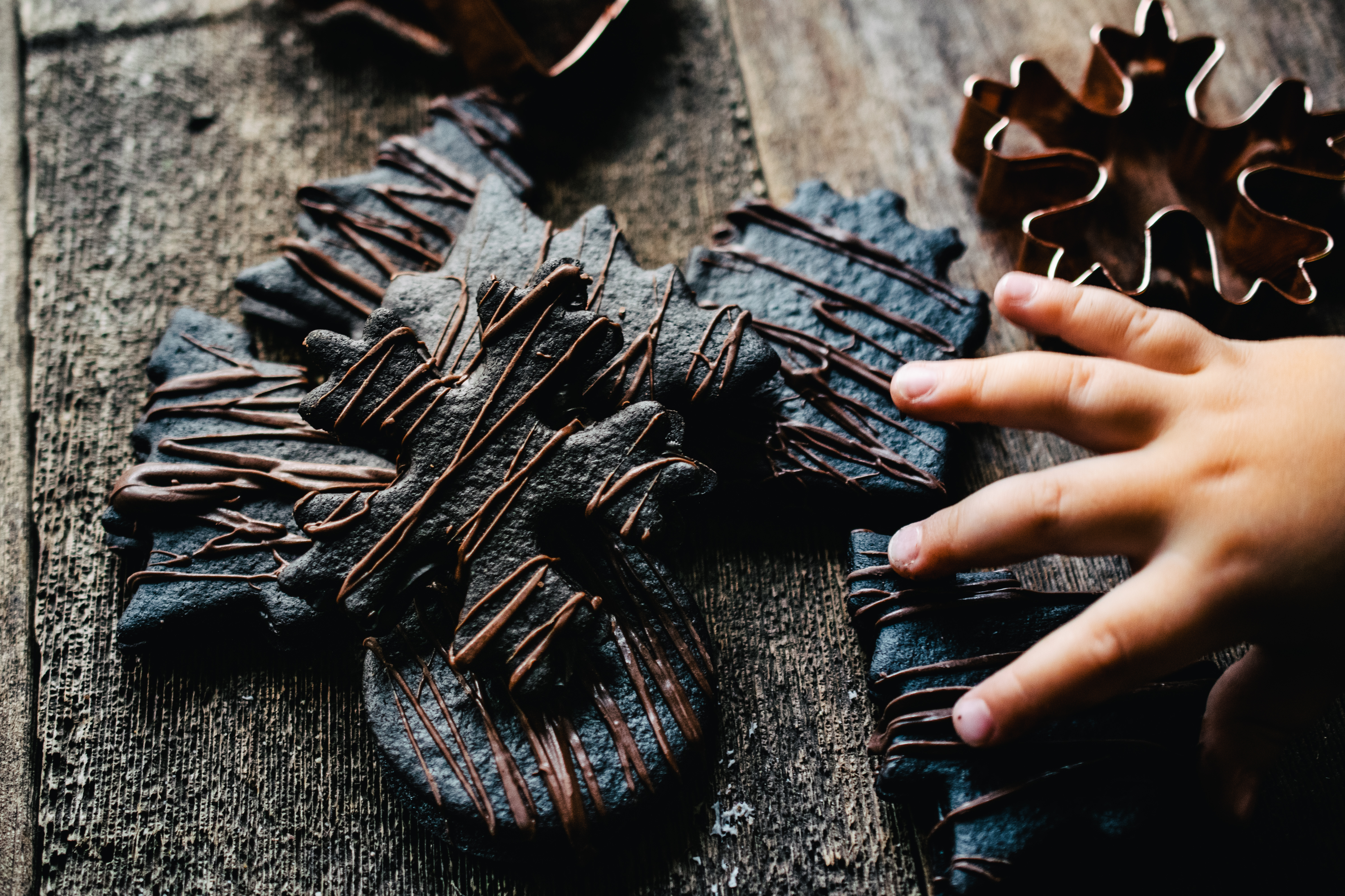 child's hand reaching for a dark chocolate holiday shaped cookie drizzled with chocolate