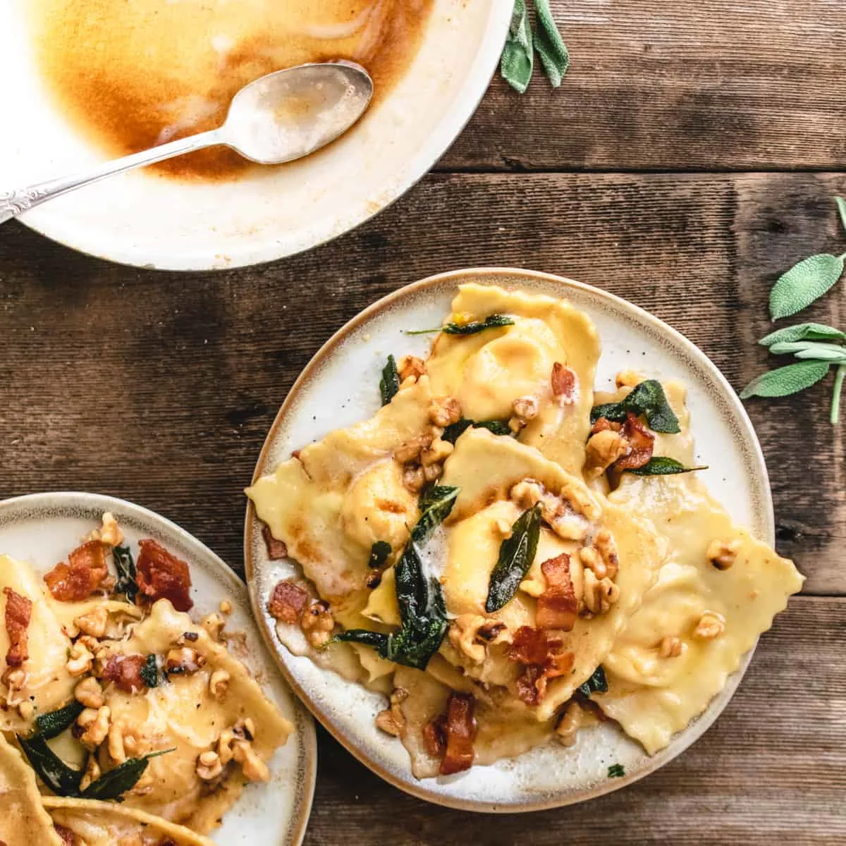 Plated ravioli topped with walnuts, sage and bacon next to pan of browned butter.