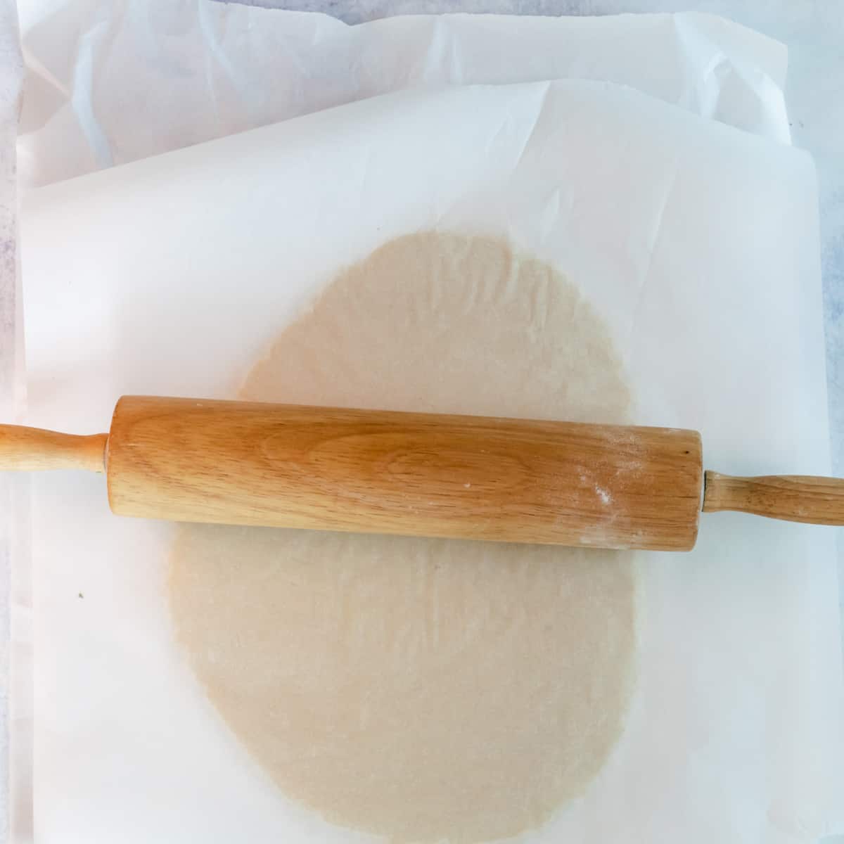 Sugar cookie dough rolled between parchment paper with a wooden rolling pin.