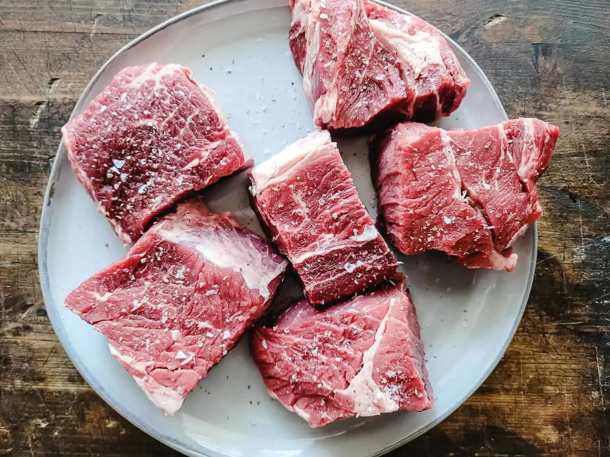 Chunks of raw chuck roast on a plate.