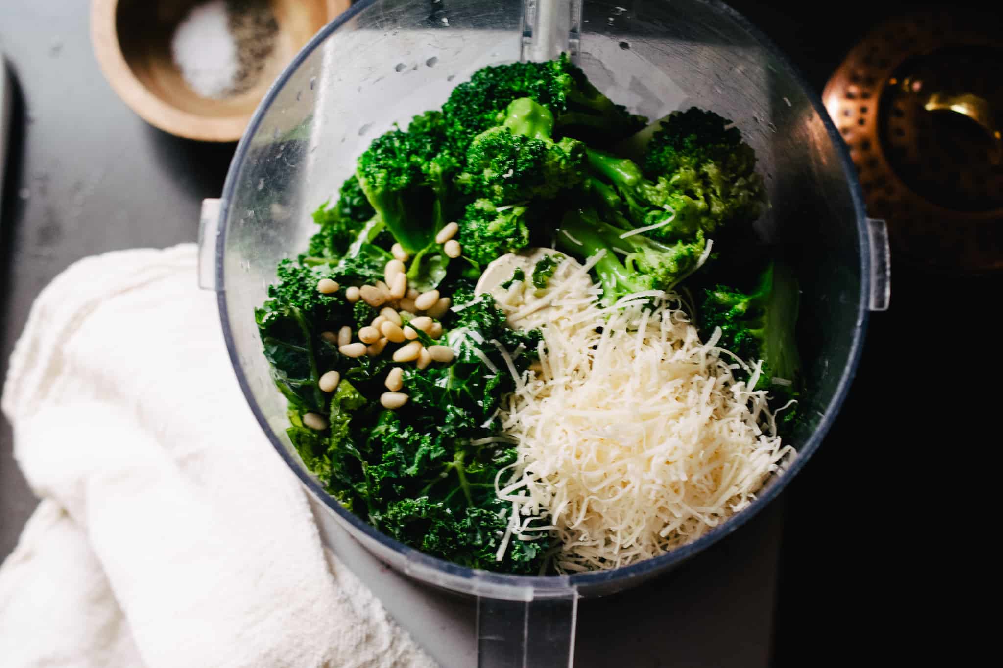 food processor with leafy greens, parmesan cheese and pine nuts