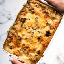 white handled casserole dish of layered sausage gravy, cheese, egg and potatoes