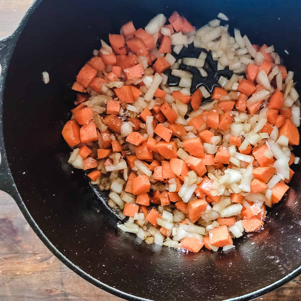 Minced onion and carrots being sautéed in a pot. 