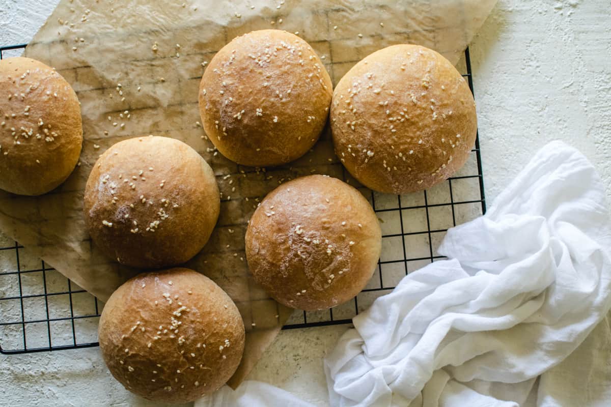 sesame seed hamburger buns on cooling rack with parchment paper and white towel 