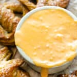 Ramekin of beer cheese surrounded by soft pretzels on brown paper.