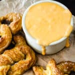 Ramekin of beer cheese by a salted soft pretzel on parchment paper.