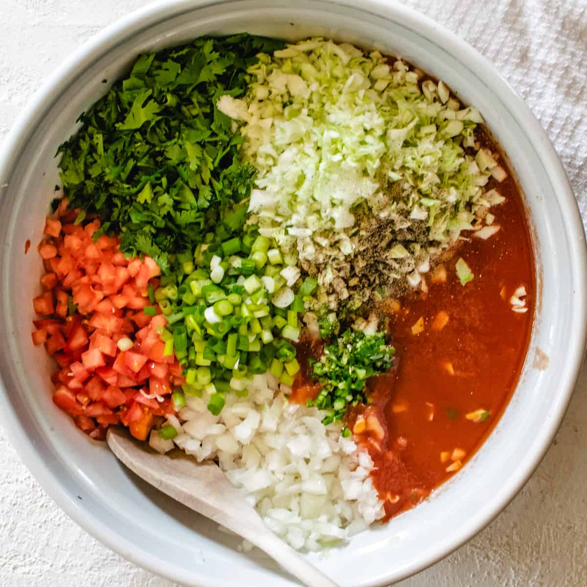 large bowl with fresh salsa ingredients including tomato juice and a wooden spoon
