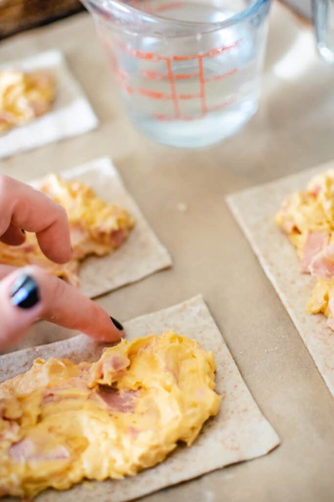 A finger dipped in water running around the edge of dough filled with ham and cheese.