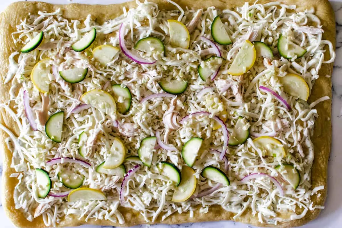 homemade pizza crust topped with ranch, zucchini, onion, garlic, chicken and mozzarella cheese