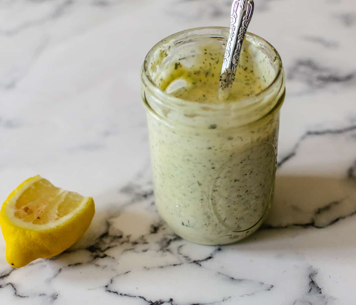 mason jar of homemade ranch sauce for pizza next to lemon wedge