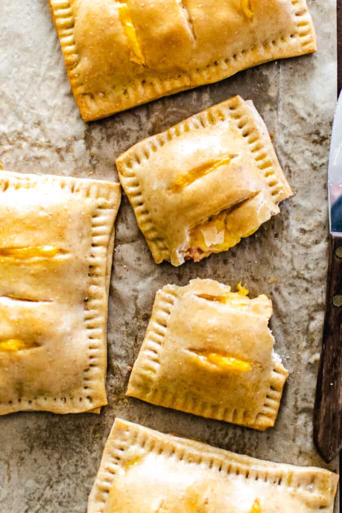 Baked rectangular pastry pouches filled with ham and cheese filling on parchment paper.