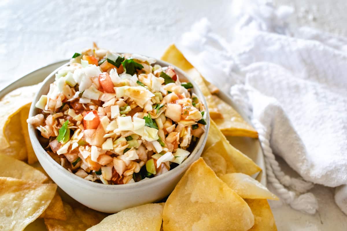 white bowl of cabbage salsa in a pile of corn tortilla chips next to white towel