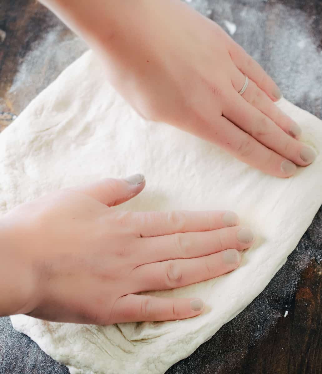 stretching pizza dough by hand on a floured surface