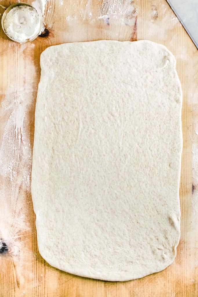 A rectangular piece of wheat dough on a floured wooden counter top.