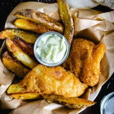 crispy homemade beer battered fish and chips with ramekin of homemade tartar sauce in brown paper basket with lemon wedges