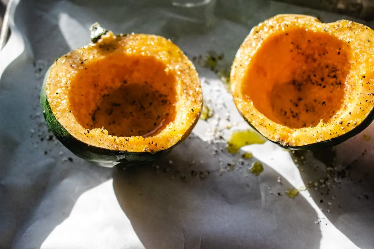 Acorn squash halves on a baking sheet drizzled with olive oil, salt and pepper.