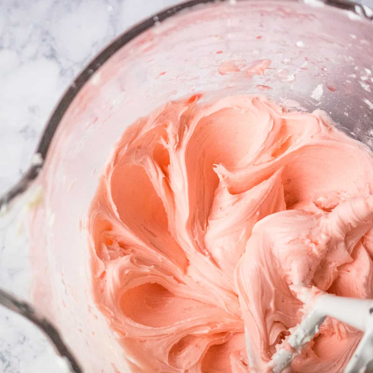 Glass mixing bowl of cherry buttercream frosting being beaten until fluffy.