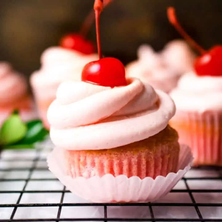 A cherry cupcake with pink cherry frosting and a cherry on top.