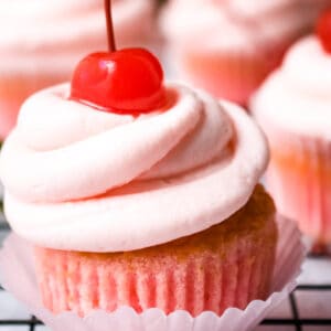A cherry cupcake with cherry frosting and a maraschino cherry on top.