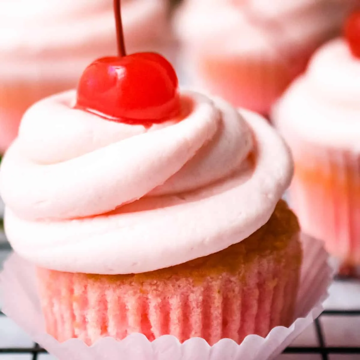 A cherry cupcake with cherry frosting and a maraschino cherry on top.