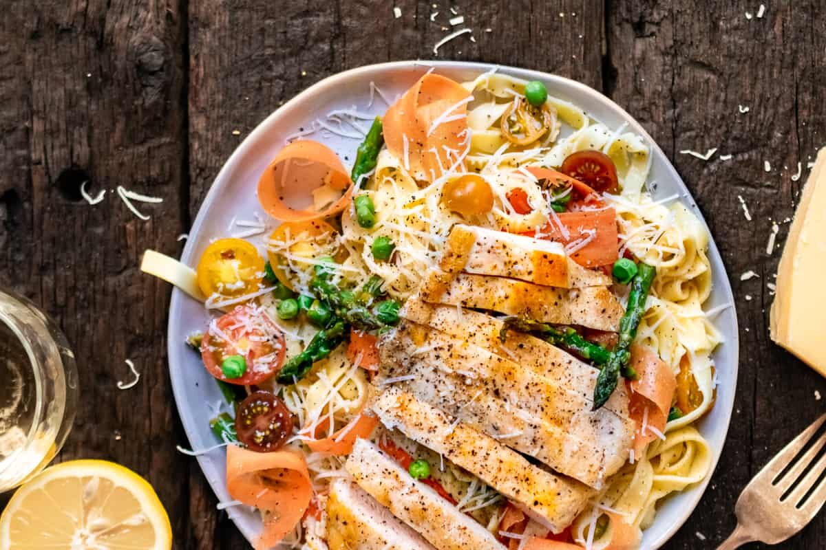 Pasta primavera on a plate with grilled chicken on top.