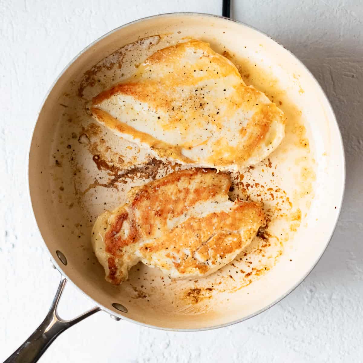 Two chicken breasts browning in a large skillet.