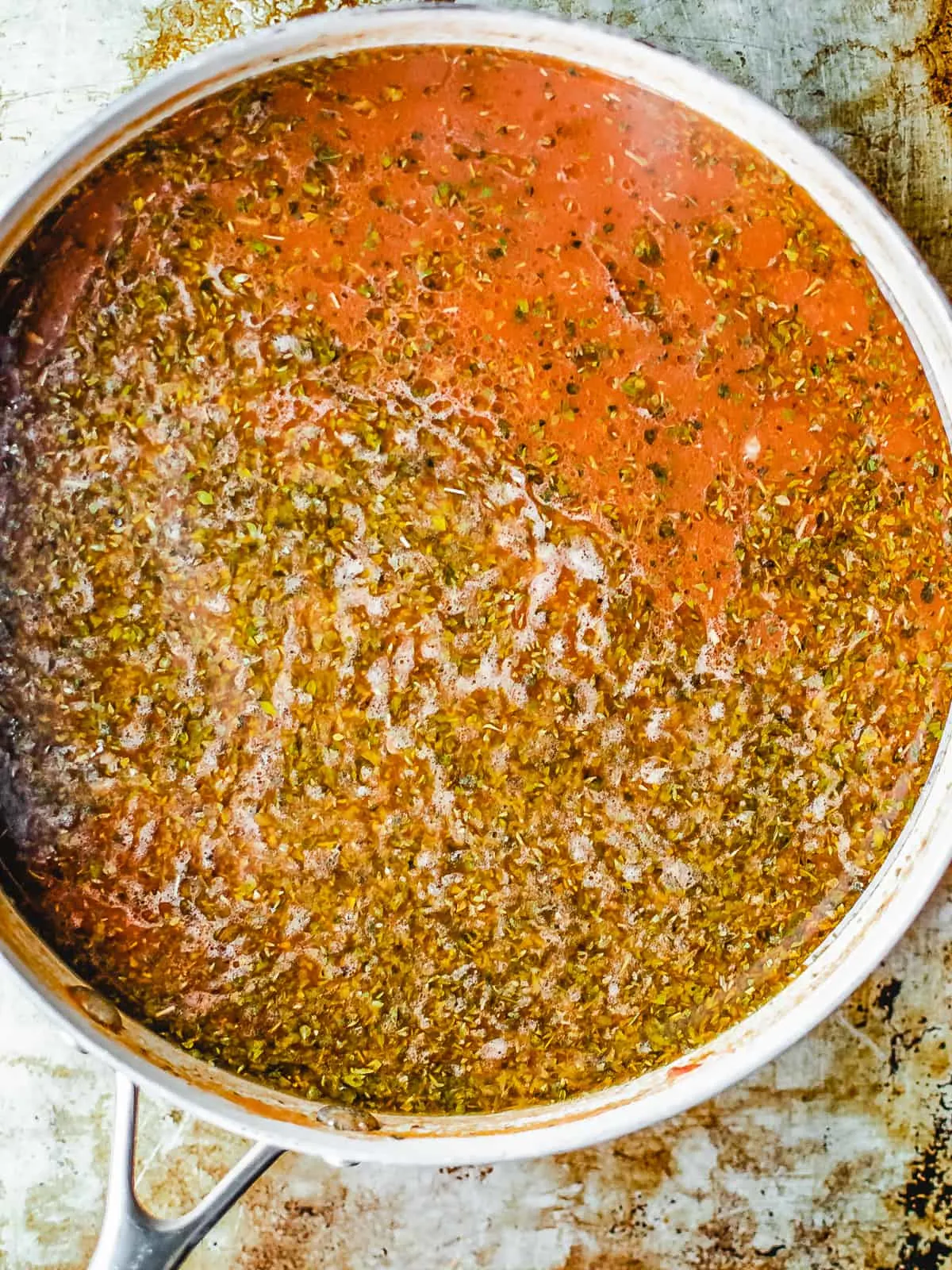 Seasonings and chicken stock in a skillet with ground beef and tomato paste.