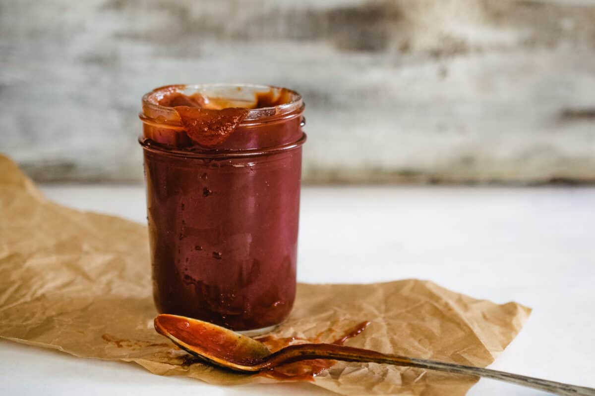 jar of homemade ketchup with spoon on brown parchment paper with distressed white wooden background