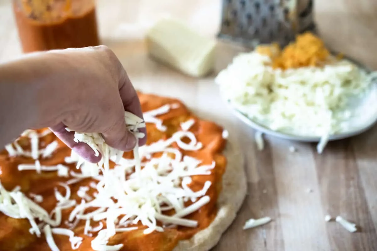 sprinkling mozzarella cheese onto homemade pizza crust with red sauce