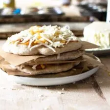 stack of small homemade pizzas between pieces of parchment paper on a plate