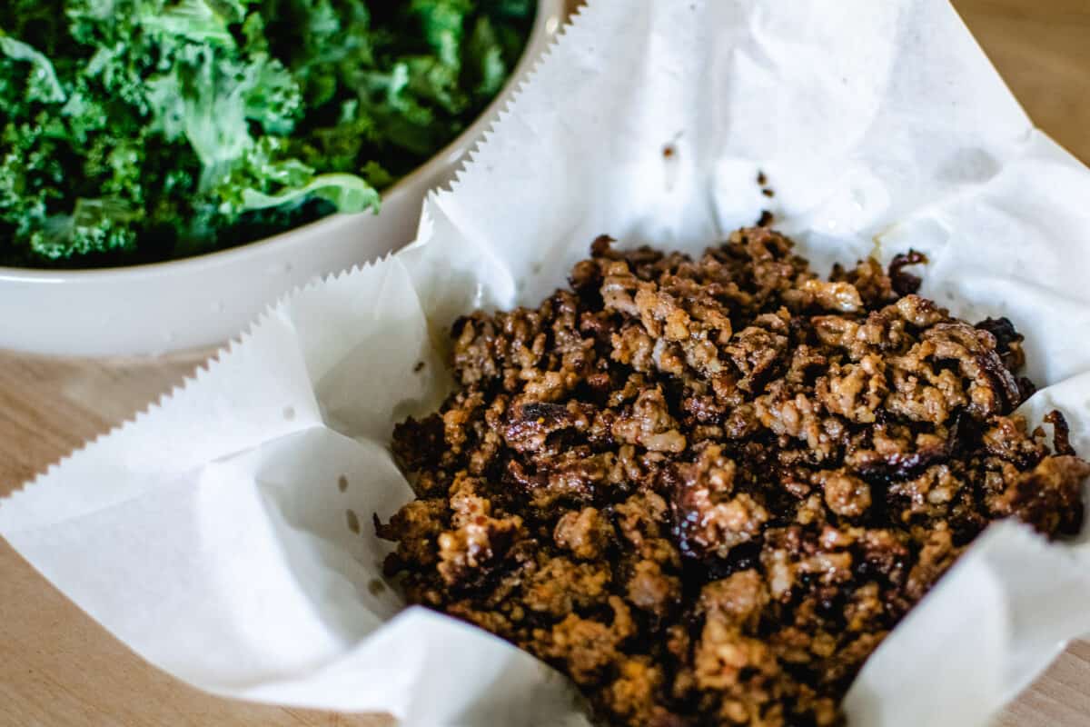 bowl of fried crispy ground sausage set aside next to chopped kale to be used in a pasta dish