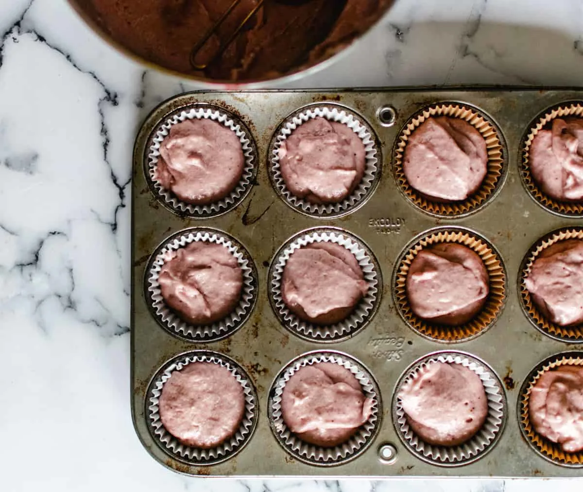 cupcake pan being filled with strawberry cupcake batter