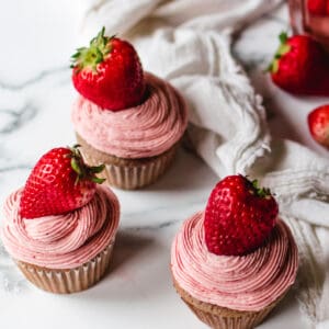 three pink strawberry cupcakes topped with strawberry frosting and fresh whole strawberry