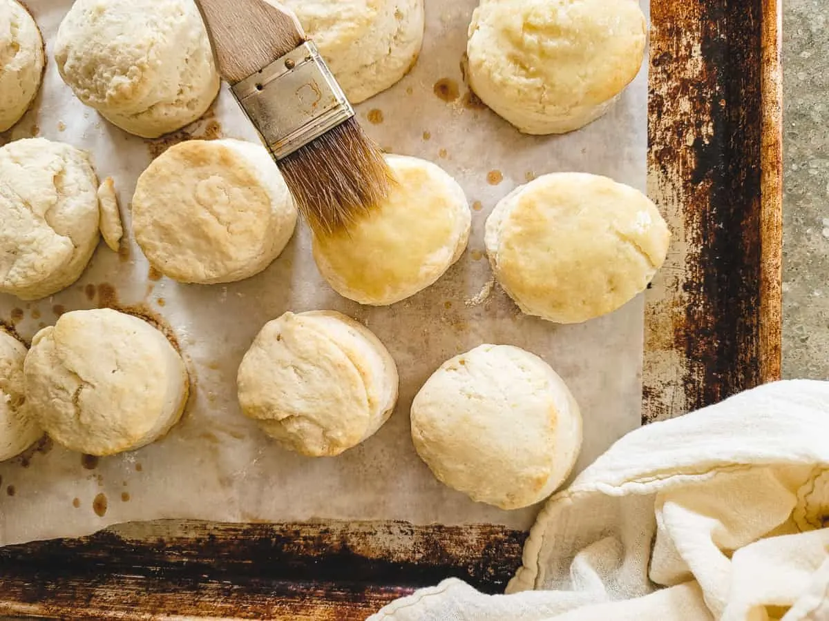 Baked biscuits on a baking sheet being brushed with melted butter.