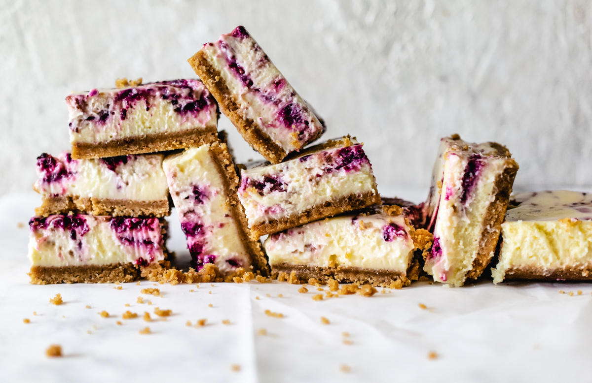 Stack of berry cheesecake bars with graham cracker crust and crumbs.