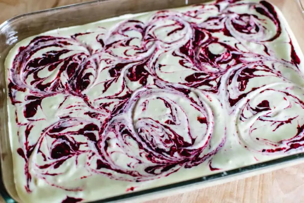 Cheesecake filling swirled with berry puree in a glass baking pan.