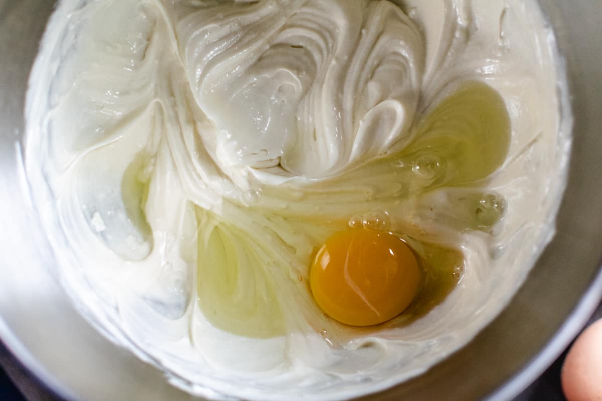 beating egg into cheesecake filling in metal bowl