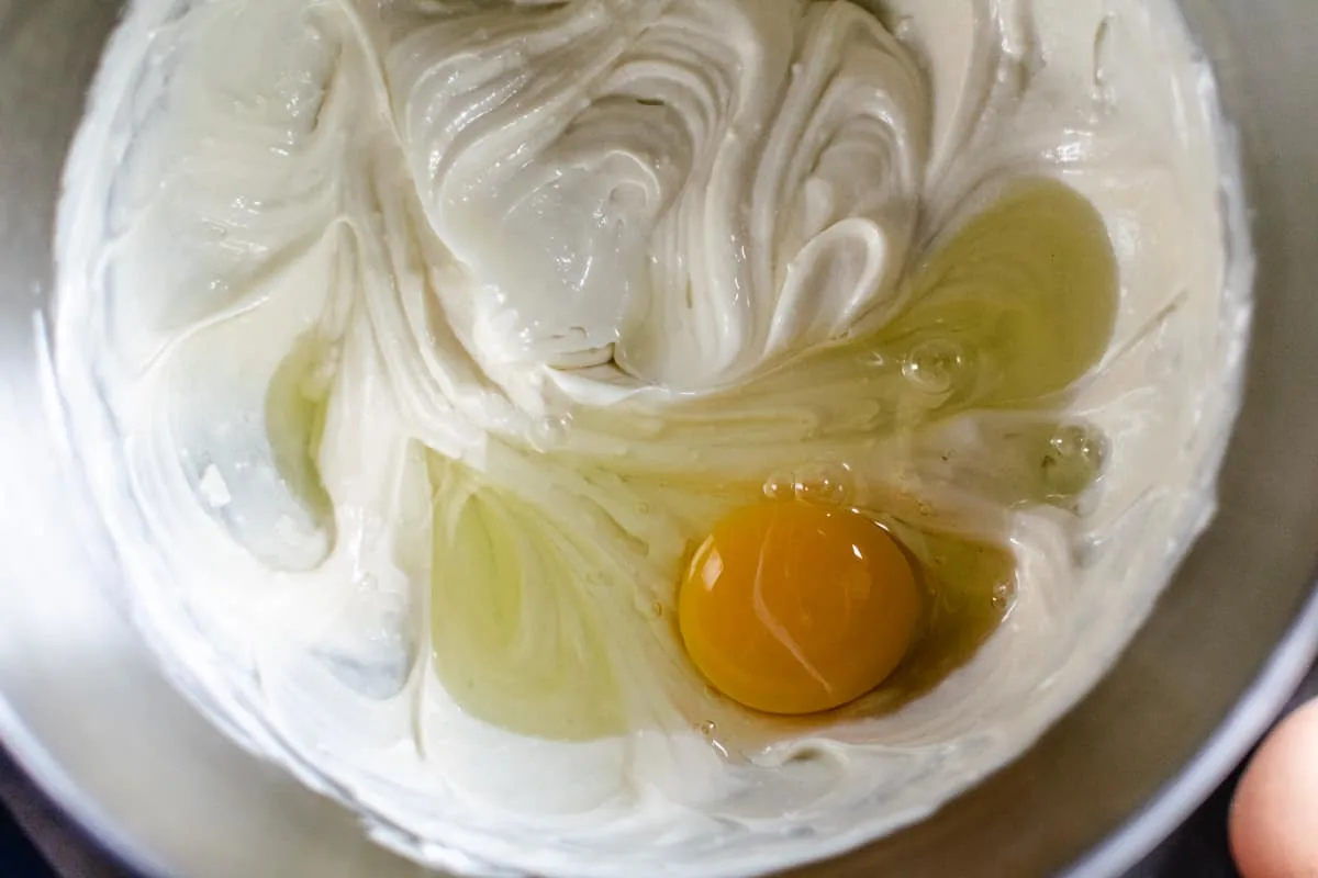 beating egg into cheesecake filling in metal bowl