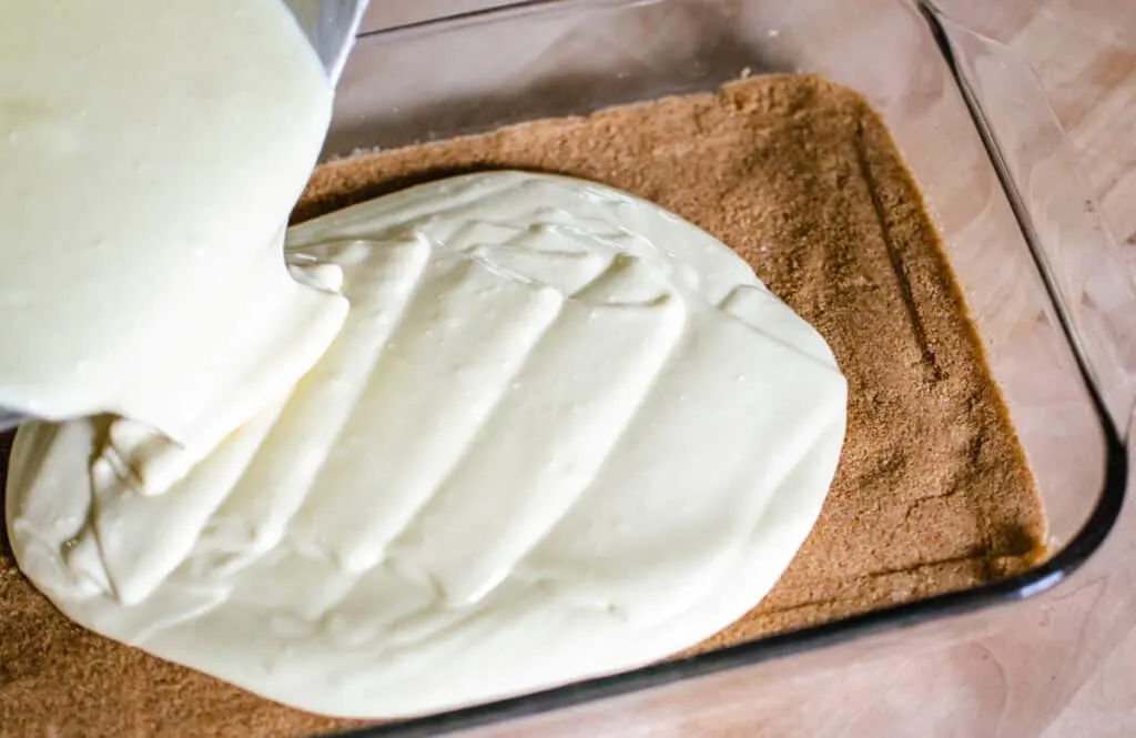 pouring half the cheesecake filling over graham cracker crust