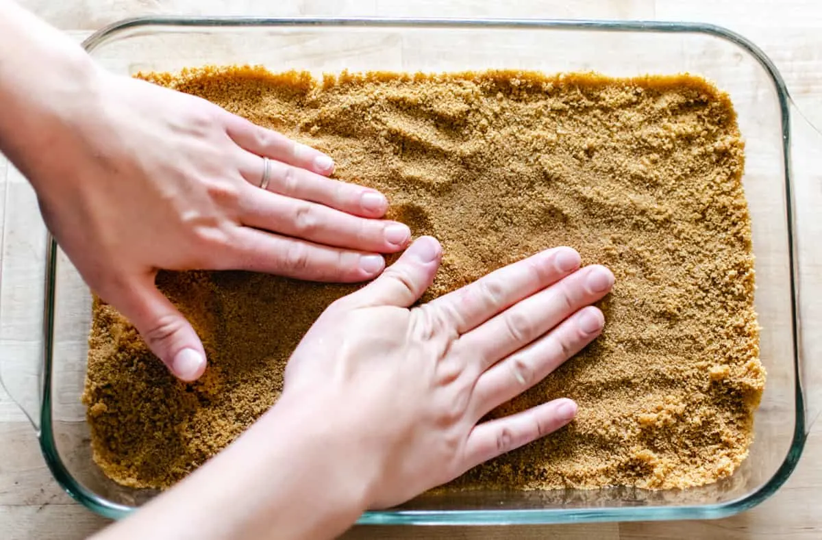 Graham cracker crust being pressed into a glass pan.