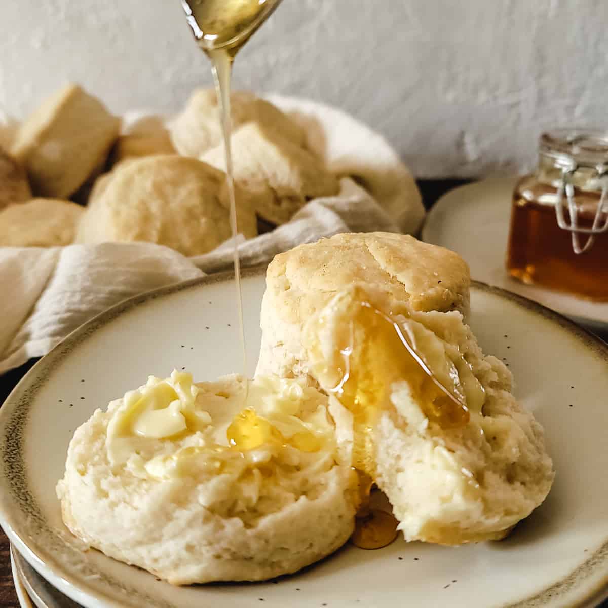 Honey drizzled over a biscuit half on a plate with butter.
