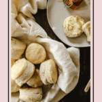 Fluffy biscuits on a towel in a bowl with butter and honey.