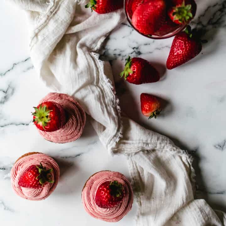 three strawberry cupcakes next to jar of fresh strawberries