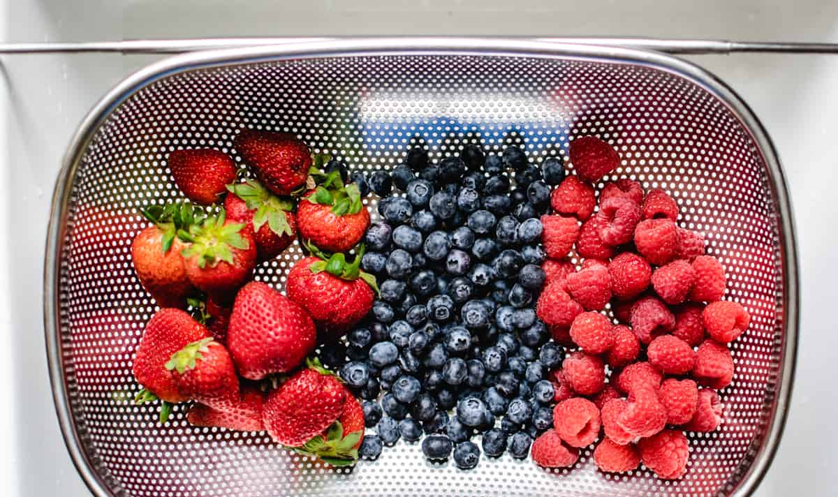 fresh strawberries, blueberries and raspberries in a strainer over the sink