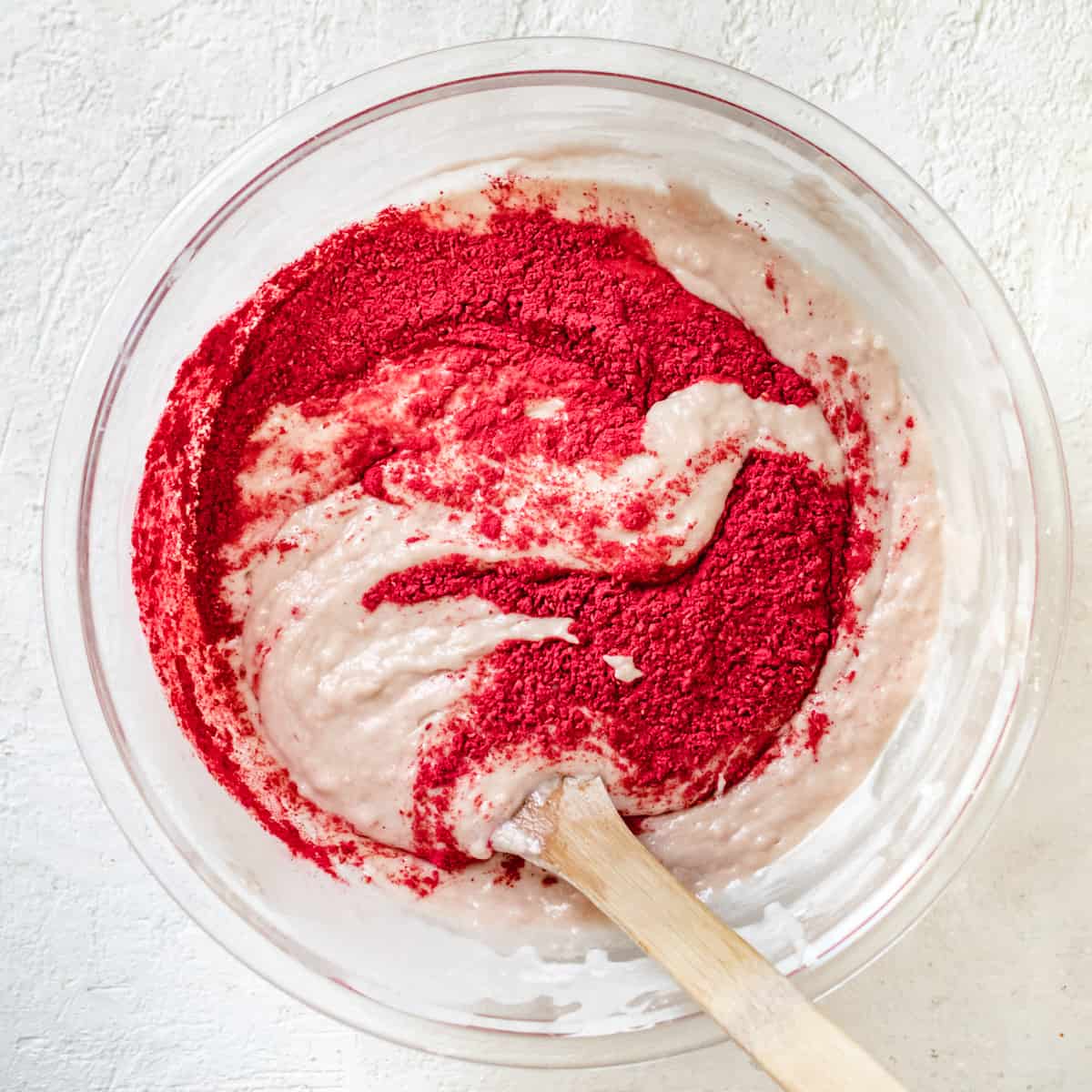 Raspberry powder folded into vanilla cupcake batter in a glass bowl.